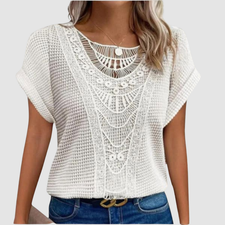 Woman in a white lace top with elegant patterns, wearing jeans, studio setting.