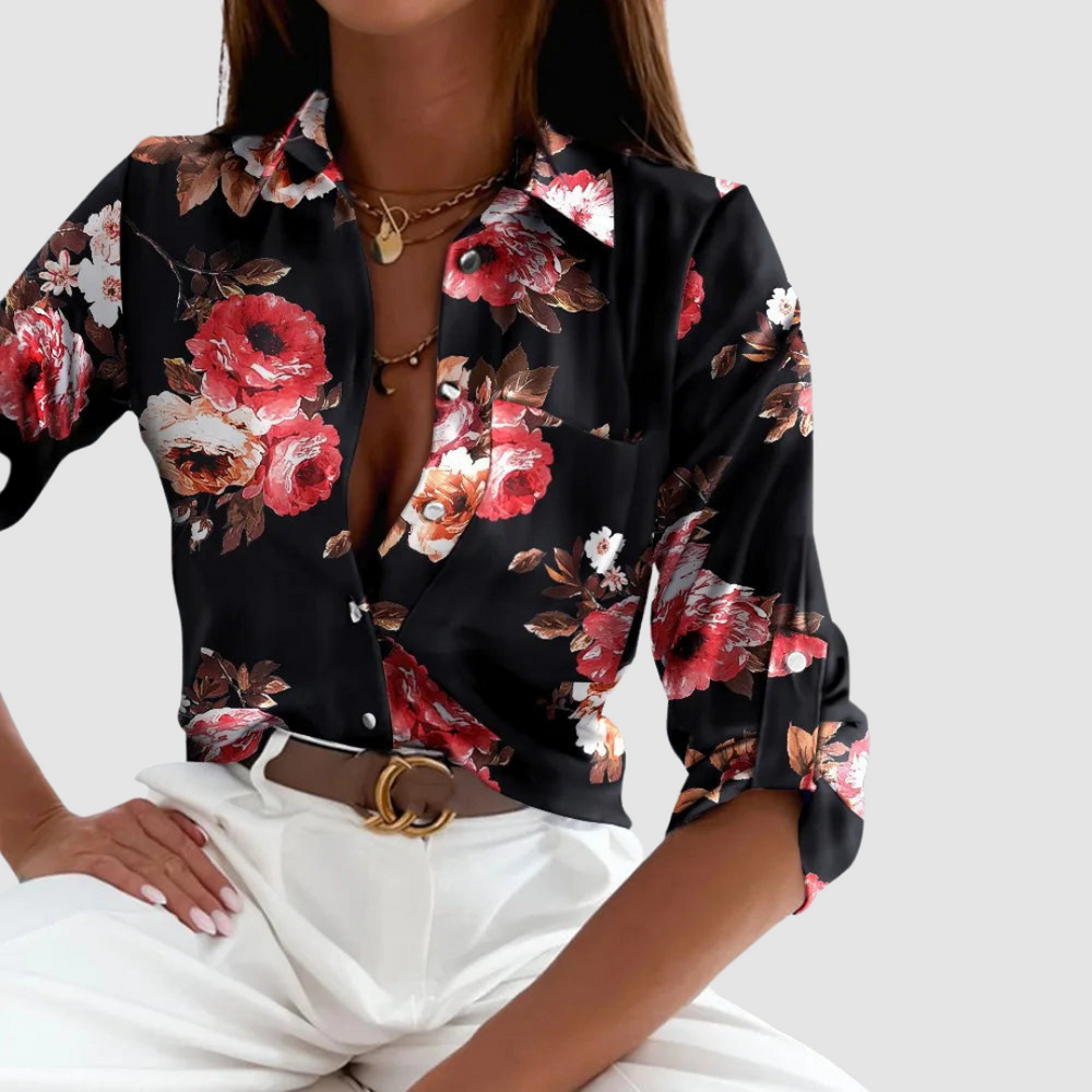 Model in a black floral blouse with red and white flowers and white pants, against a plain backdrop.