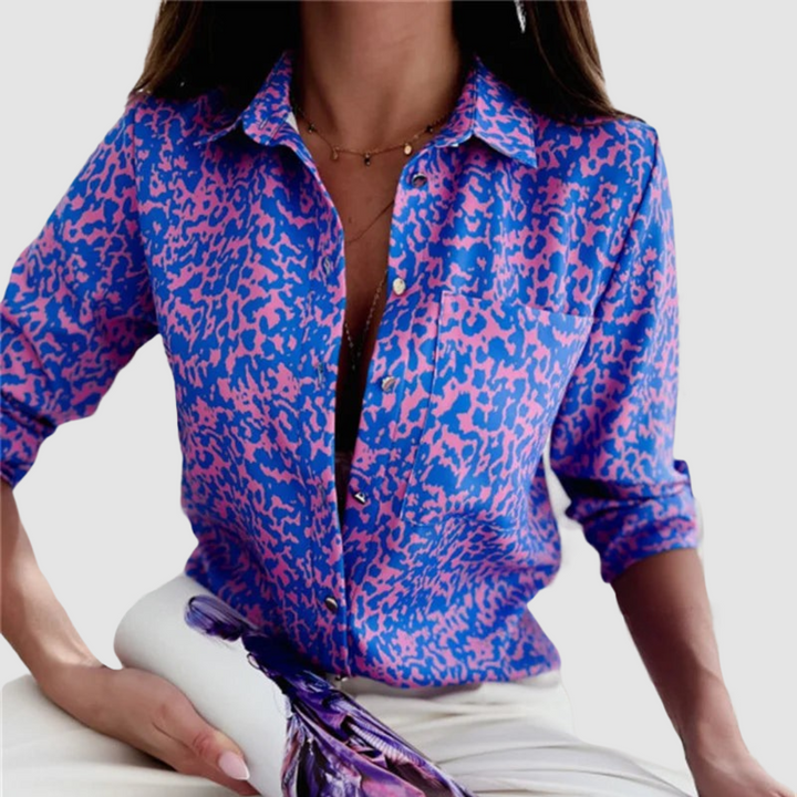 Model wearing a blue and pink patterned blouse with white pants, against a white background.