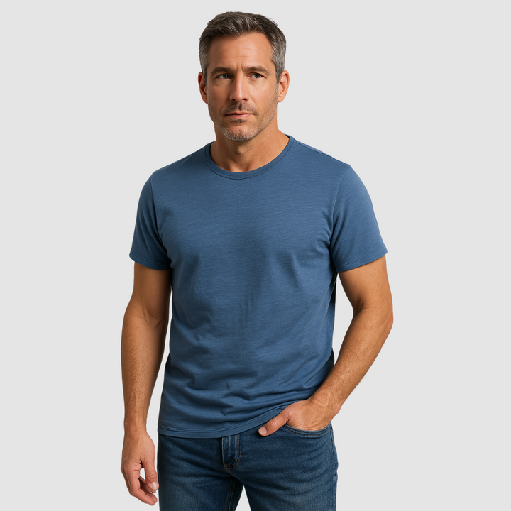 Man wearing a blue short-sleeve t-shirt with a round neck, paired with jeans, studio setting.