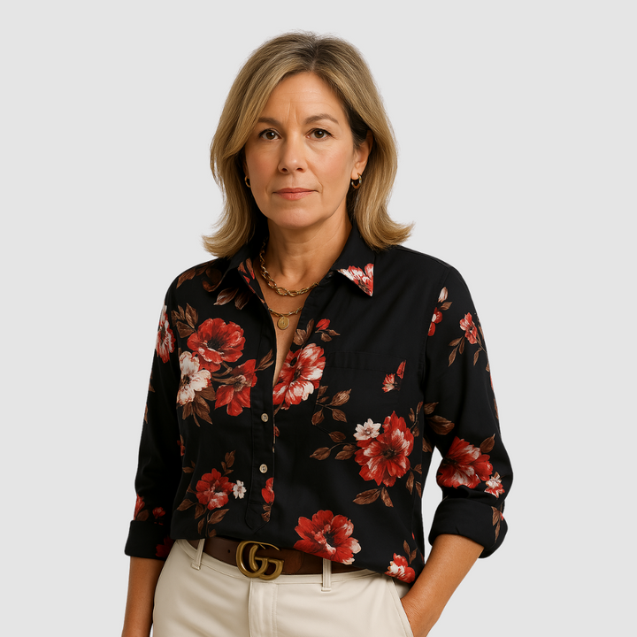 Woman wearing a black floral blouse with red and white flowers, set against a plain background.