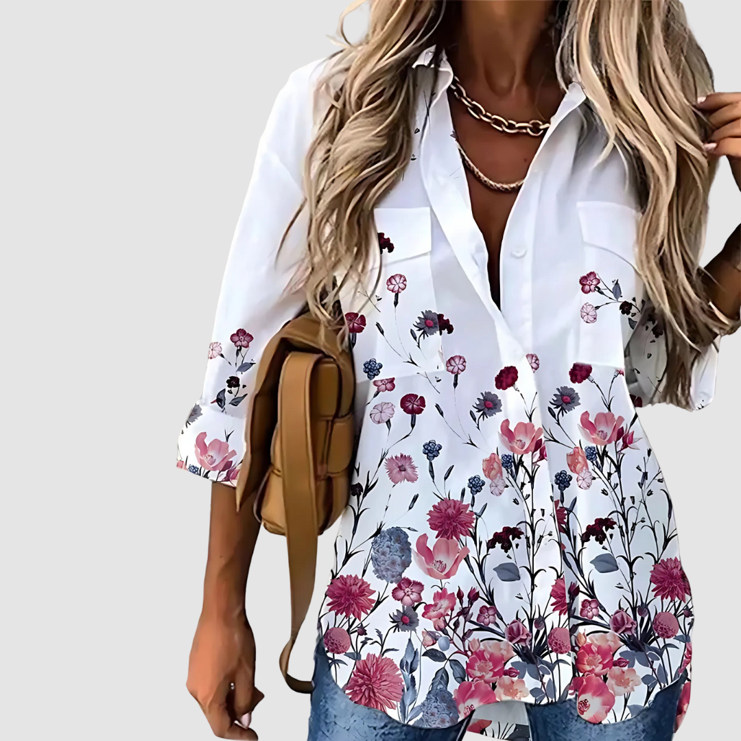 White blouse with rich pink, red, and blue floral pattern, styled with jeans and a plain background.