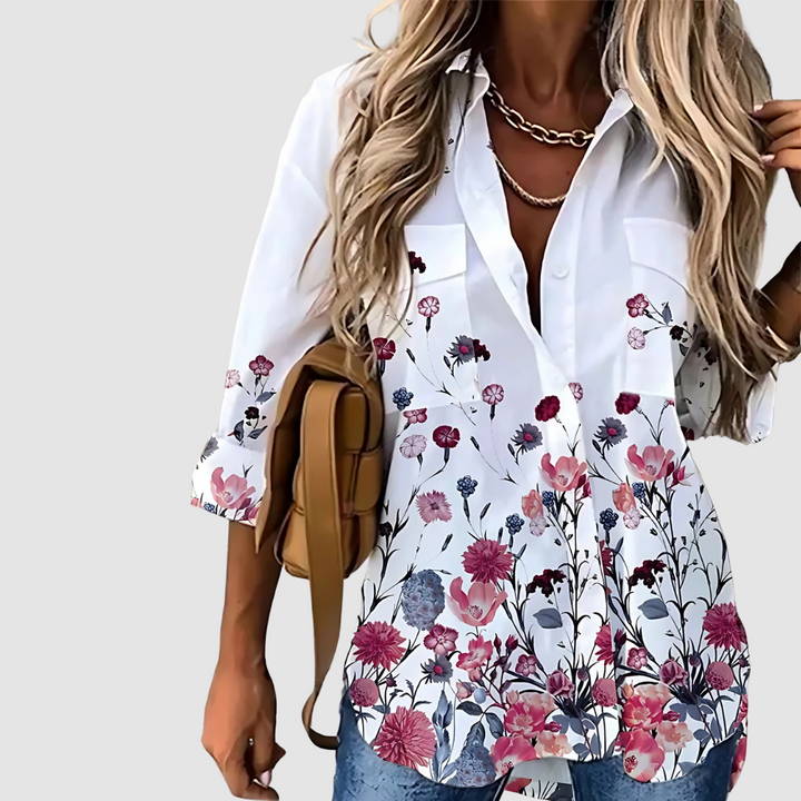 White blouse with rich pink, red, and blue floral pattern, styled with jeans and a plain background.