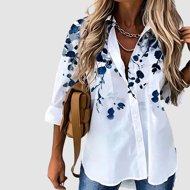 White blouse adorned with deep blue abstract floral print, worn with jeans on a plain background.