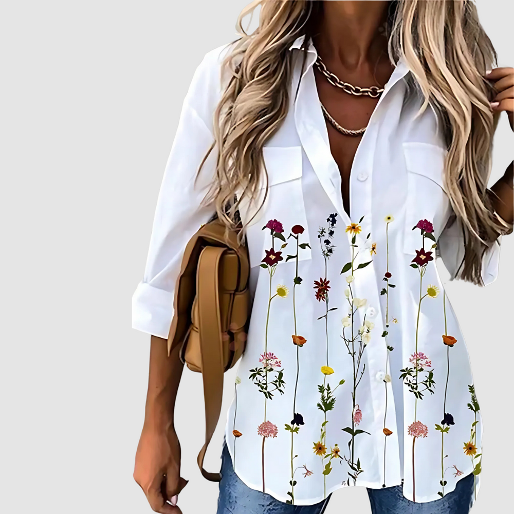 White blouse featuring vibrant vertical floral design, paired with jeans against a plain backdrop.
