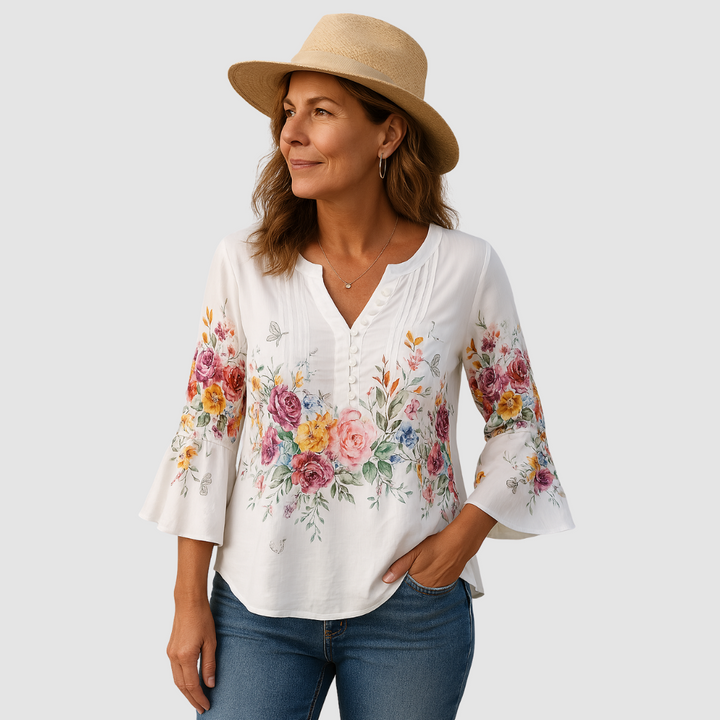Woman in floral blouse with bell sleeves, wearing jeans and a hat, set in a studio with white background.
