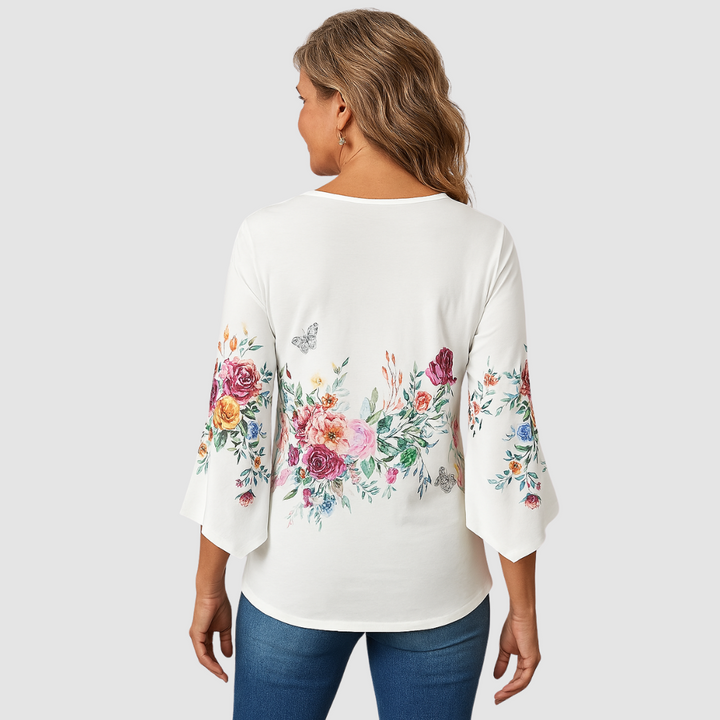 Back view of a woman wearing a floral blouse with bell sleeves, jeans, in a studio with white background.