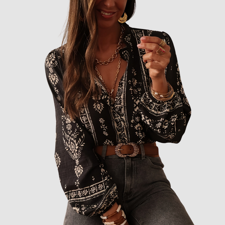 Model in black boho blouse with white floral print, accessorized with gold jewelry and vintage belt. Studio background.