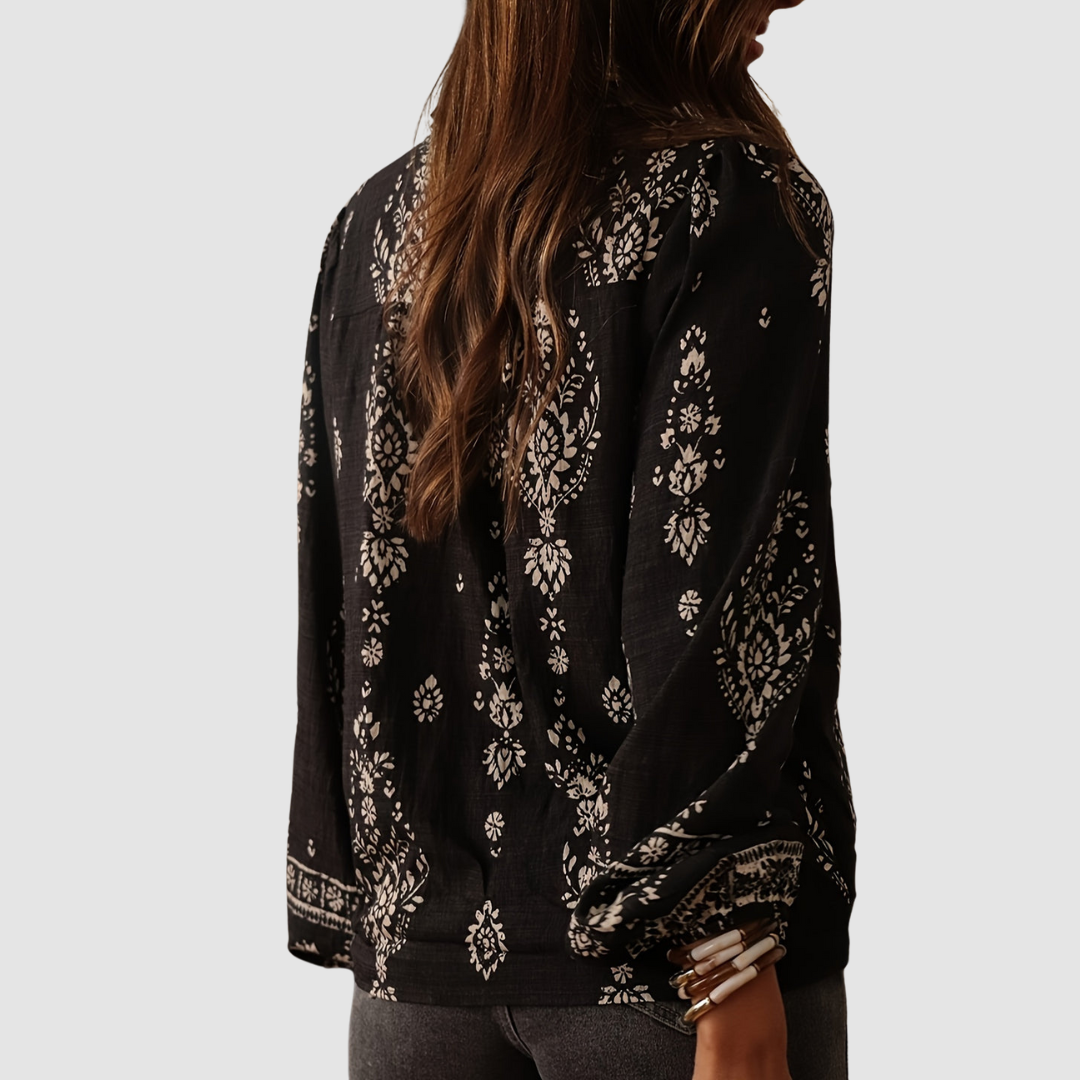 Back view of black boho blouse with white floral designs, highlighting relaxed fit. Studio background.