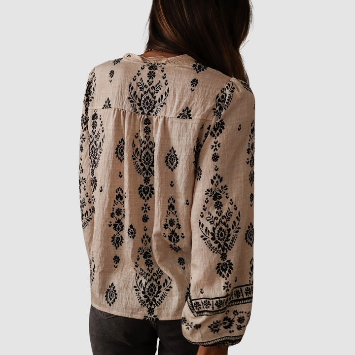 Back view of a beige boho blouse with black floral patterns, showing relaxed fit and intricate print. Studio background.