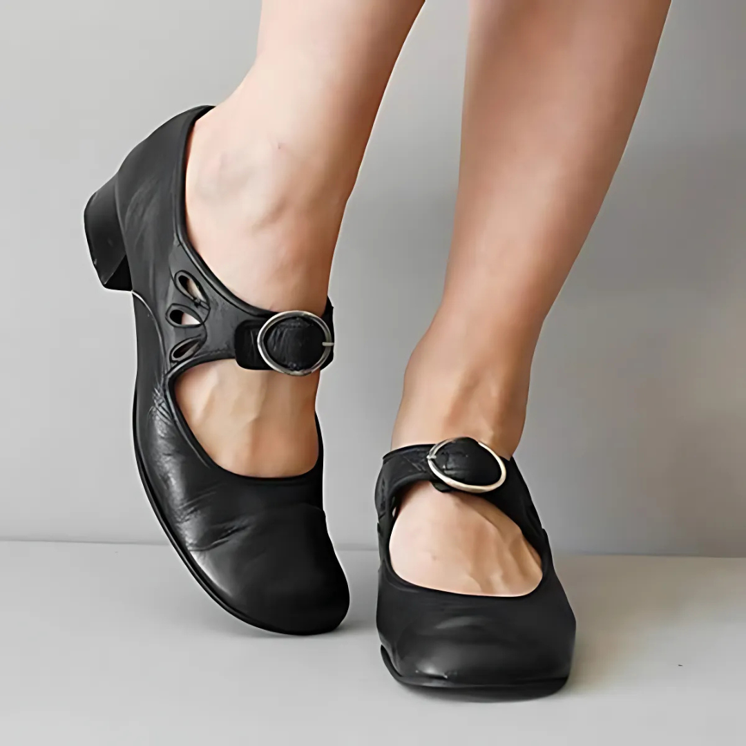Black leather sandals with buckle detail shown from the front on feet against a neutral background.