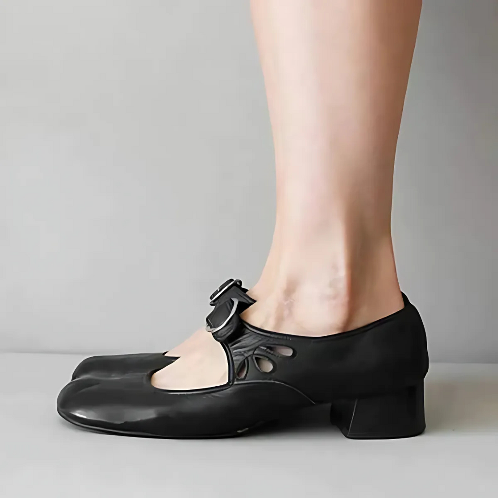 Side view of black leather sandals with buckle on feet in a neutral setting.