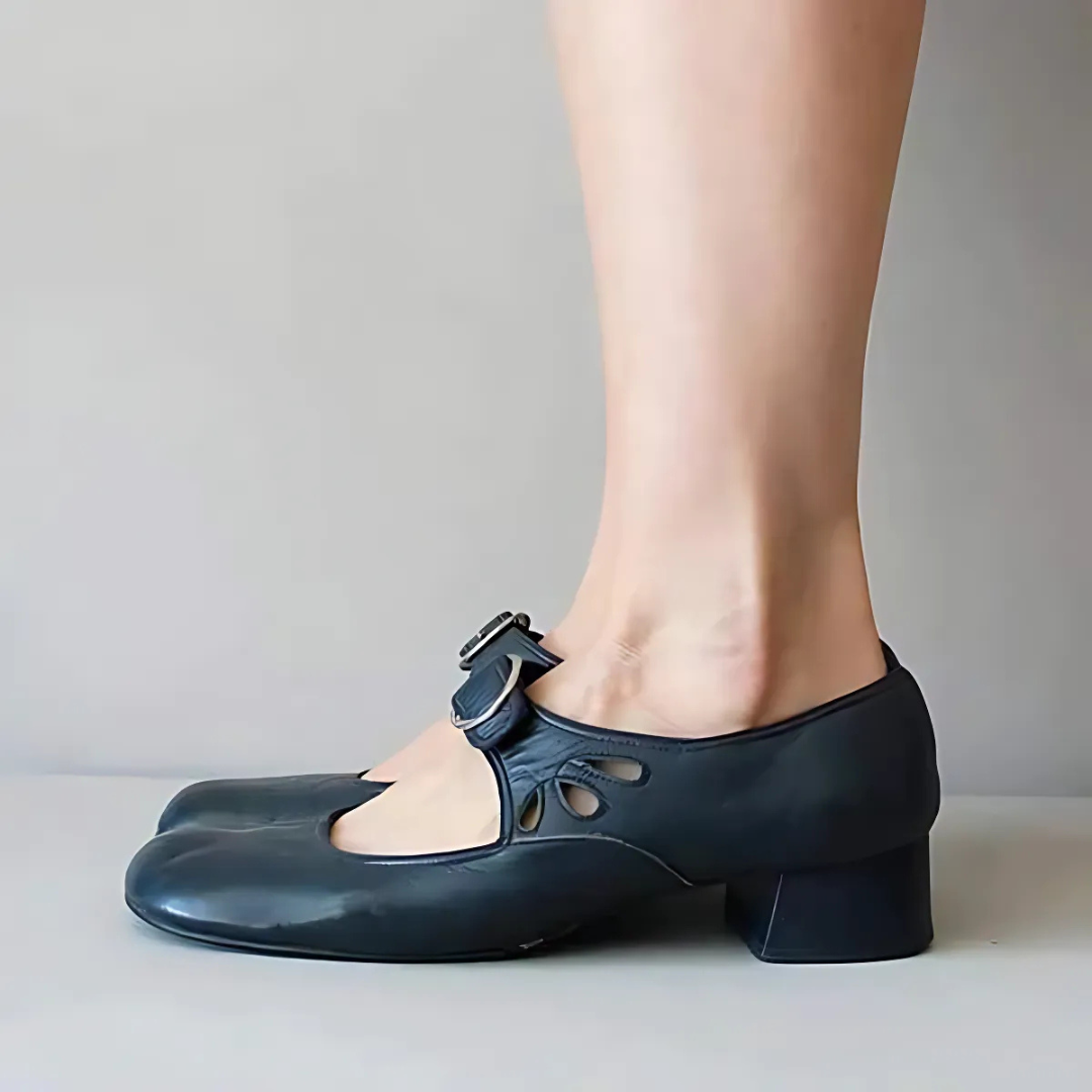 Side view of black leather sandals with buckle on feet in an elegant setting.