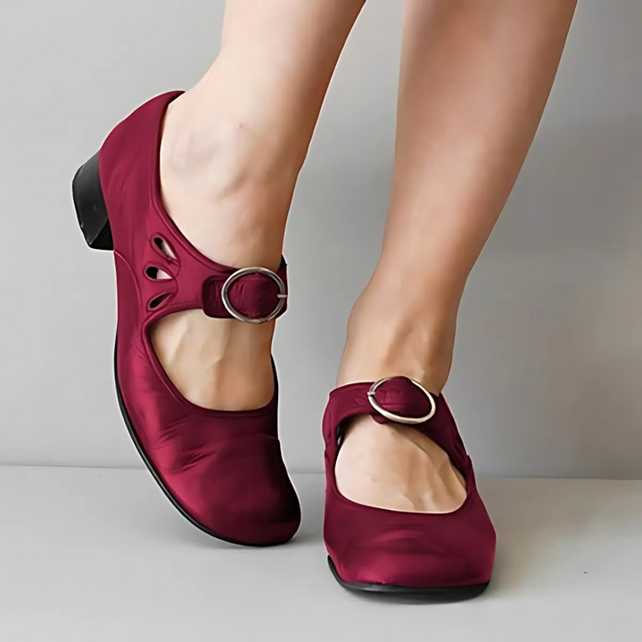 Burgundy leather sandals with buckle detail shown from the front on feet against a neutral background.