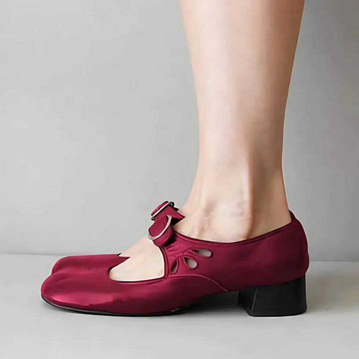 Side view of burgundy leather sandals with buckle on feet in a neutral setting.
