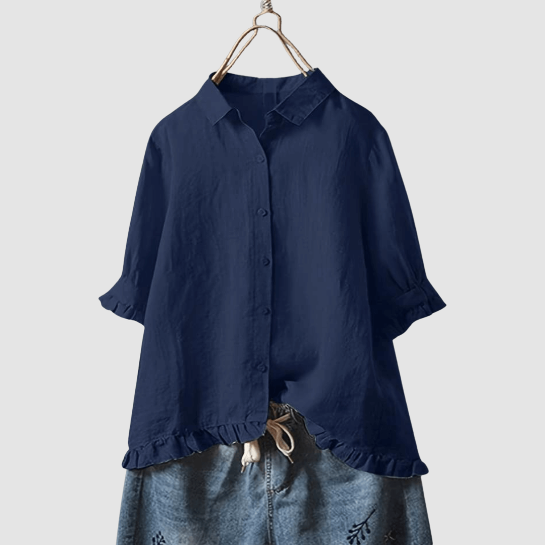 Navy blue blouse with button-front, three-quarter sleeves, and ruffled hem, paired with denim shorts on a hanger against a gray background.