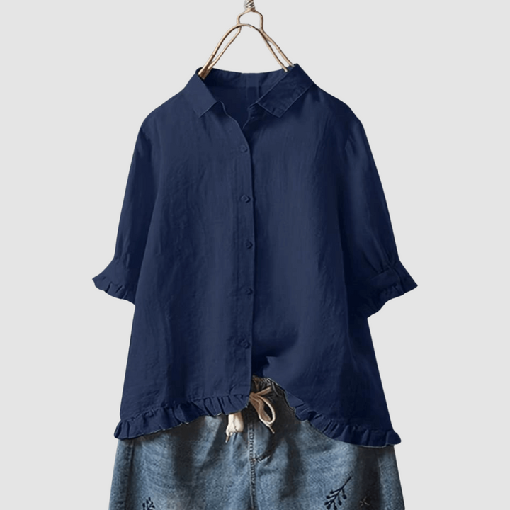 Navy blue blouse with button-front, three-quarter sleeves, and ruffled hem, paired with denim shorts on a hanger against a gray background.