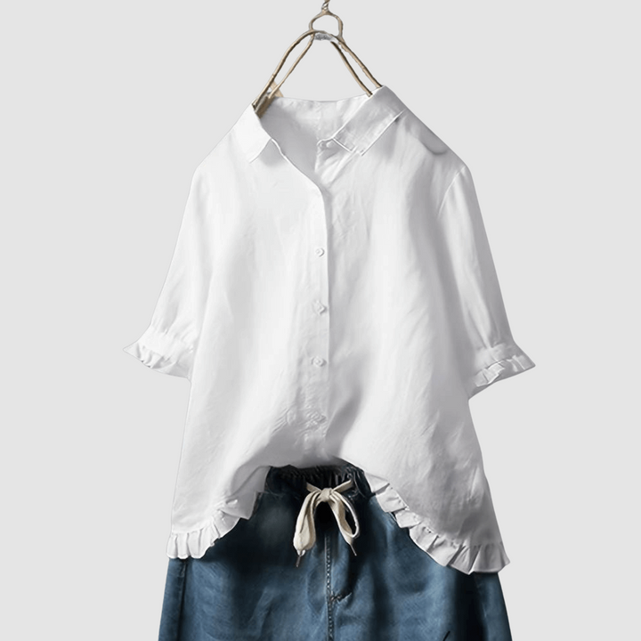 White blouse with button-front, three-quarter sleeves, and ruffled hem, paired with denim shorts on a hanger against a gray background.