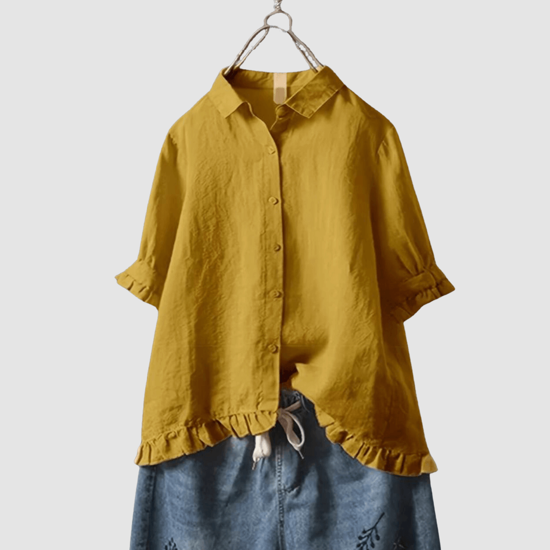 Yellow blouse with button-front, three-quarter sleeves, and ruffled hem, paired with denim shorts on a hanger against a gray background.