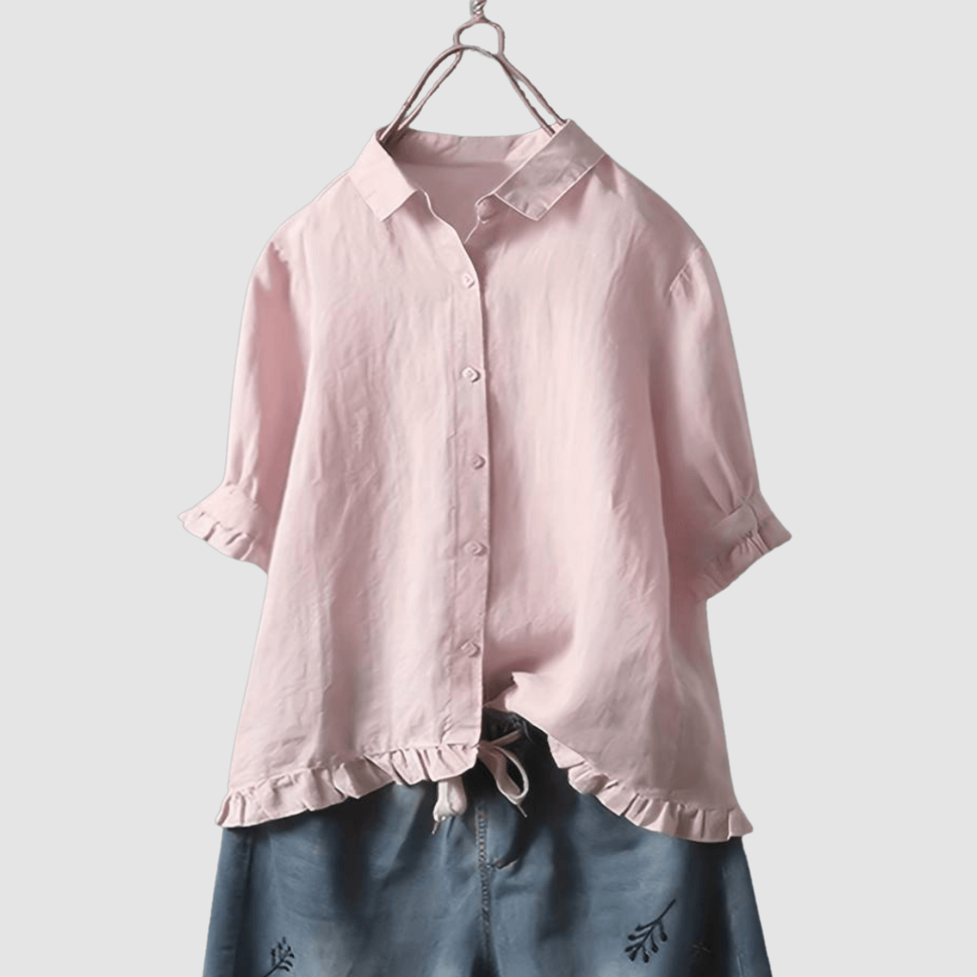 Light pink blouse with button-front, three-quarter sleeves, and ruffled hem, paired with denim shorts on a hanger against a gray background.
