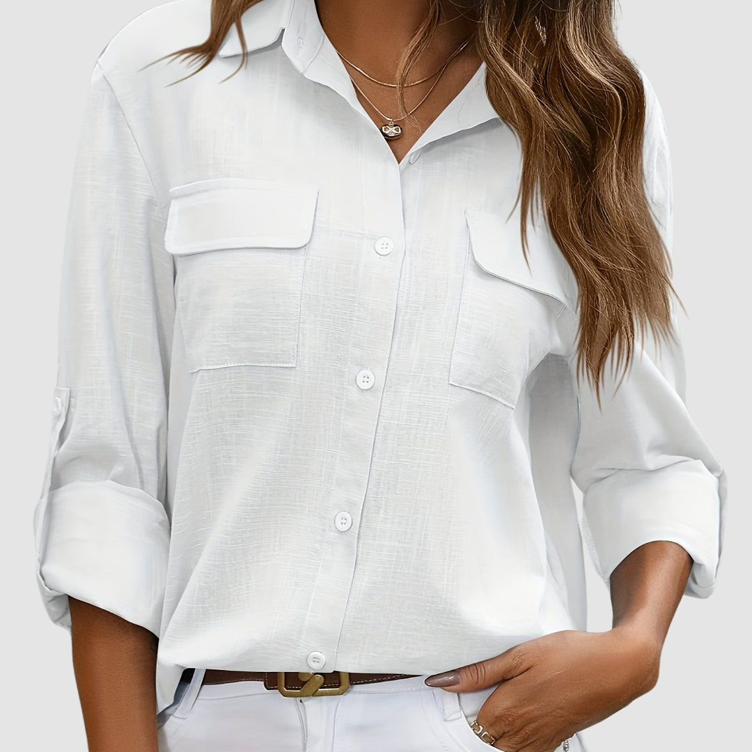 White pocket blouse with rolled sleeves, two front pockets, worn with necklaces, studio setting.