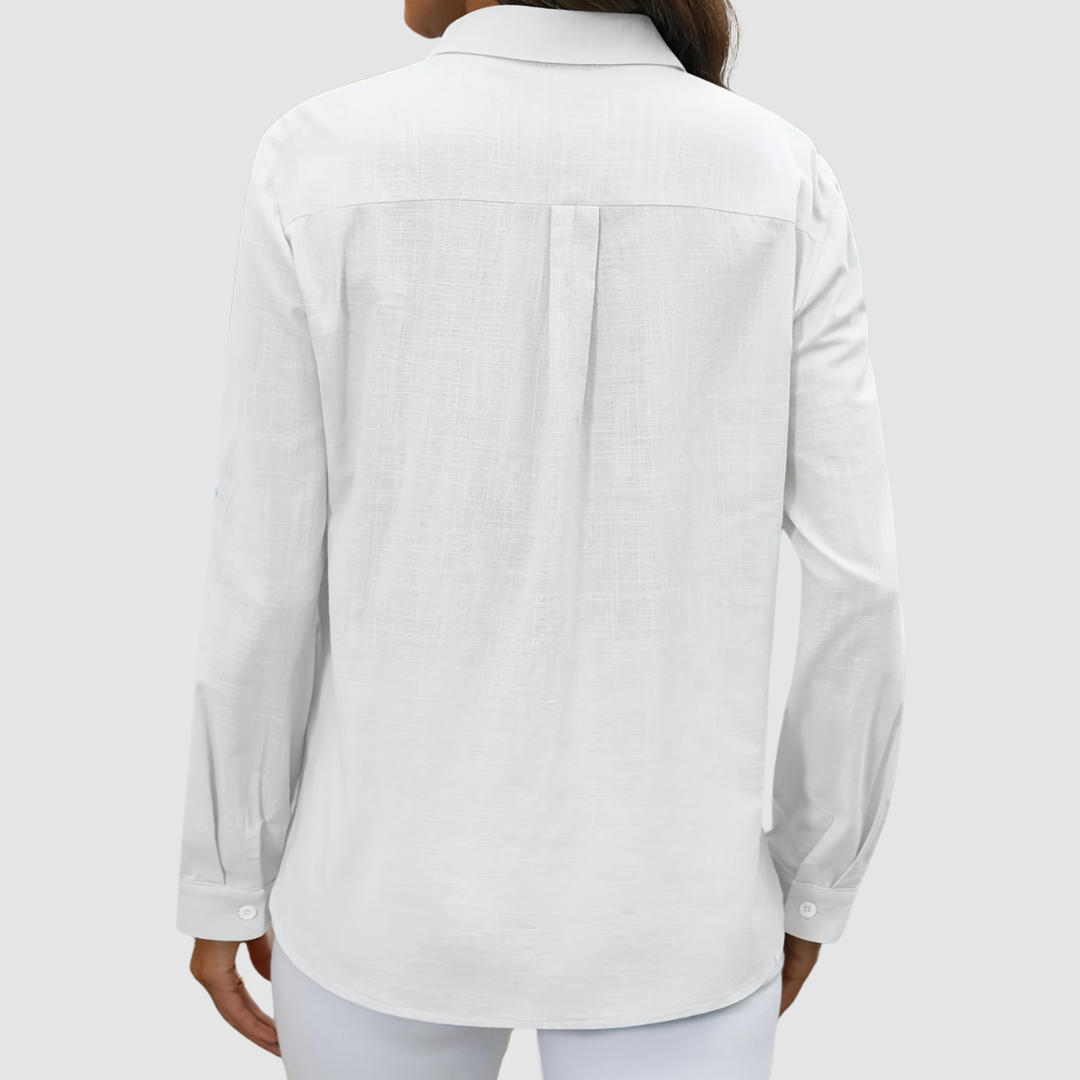Back view of white blouse with pleat detail and buttoned cuffs, studio setting.