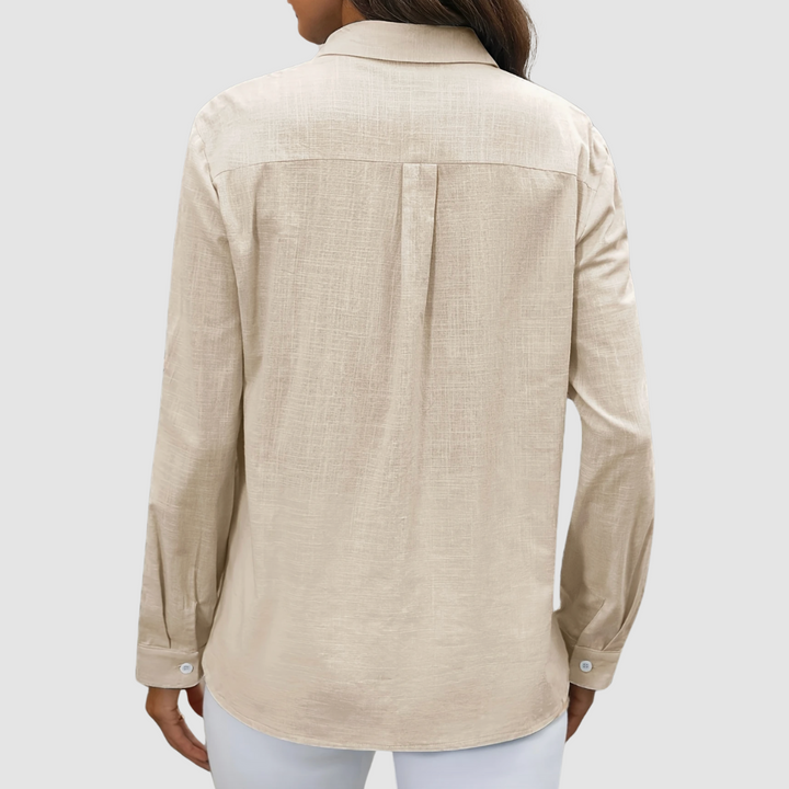 Back view of beige blouse with pleat detail and buttoned cuffs, studio setting.