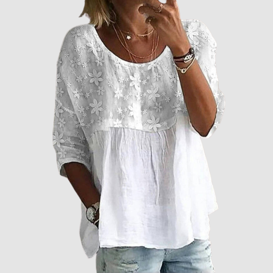 Woman wearing a loose fit, white floral patterned shirt with rolled-up sleeves and distressed jeans in a casual pose against a light gray background.