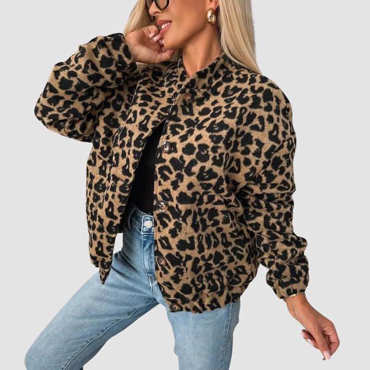 Woman posing in leopard print jacket and jeans, smiling, with a light background.