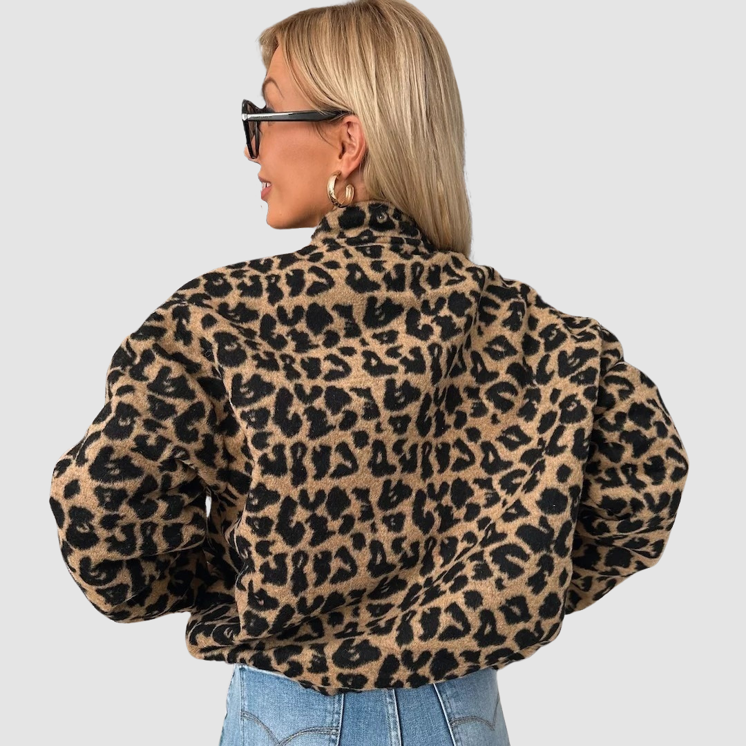 Back view of woman in leopard print jacket and blue jeans, light background.