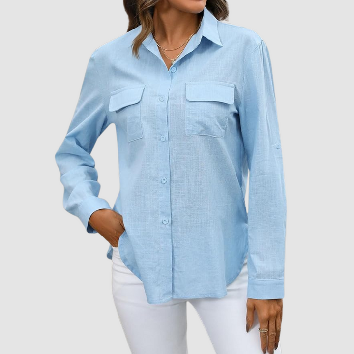 Light blue pocket blouse with long sleeves and front pockets, hand in pocket, studio background.
