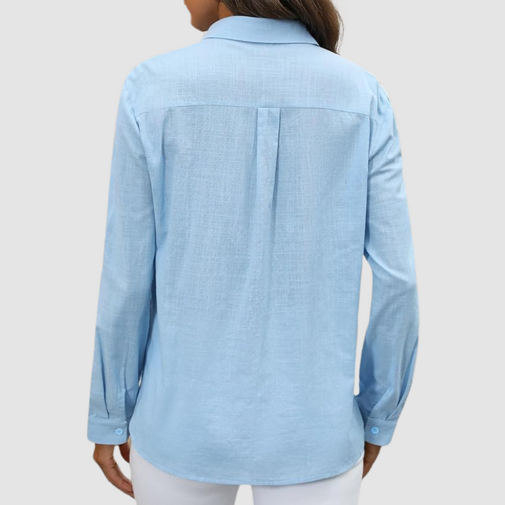 Back view of light blue blouse with pleat detail and buttoned cuffs, studio setting.