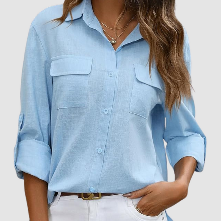 Light blue pocket blouse with rolled sleeves, two front pockets, worn with necklaces, studio setting.