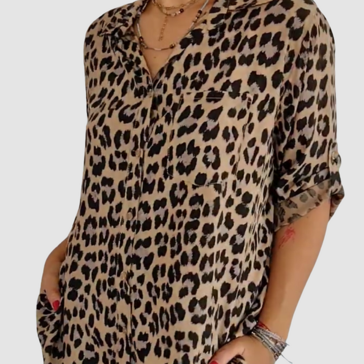Woman wearing a beige leopard print blouse with hands in pockets. Studio background.