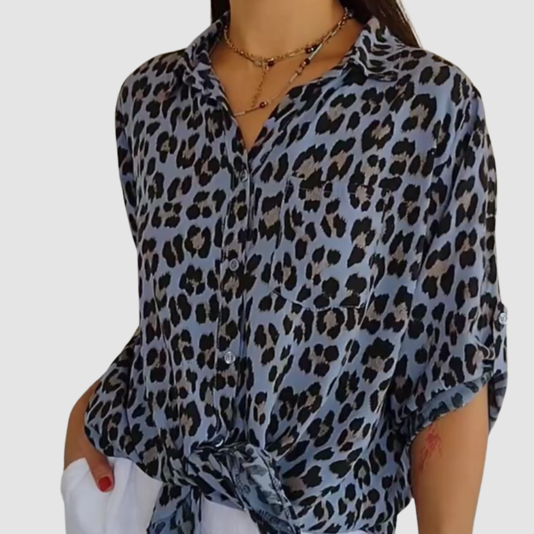 Woman in a blue leopard print blouse tied at the waist with short sleeves. Studio background.