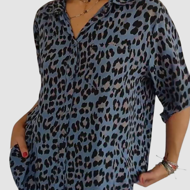 Close-up of a woman in a blue leopard print blouse with short sleeves. Studio background.
