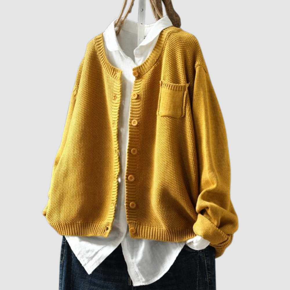 Mustard knit cardigan on hanger over white shirt and dark jeans against a light gray background.