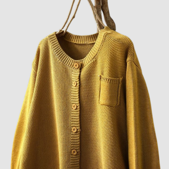 Close-up of mustard knit cardigan on hanger with button detail, light gray background.