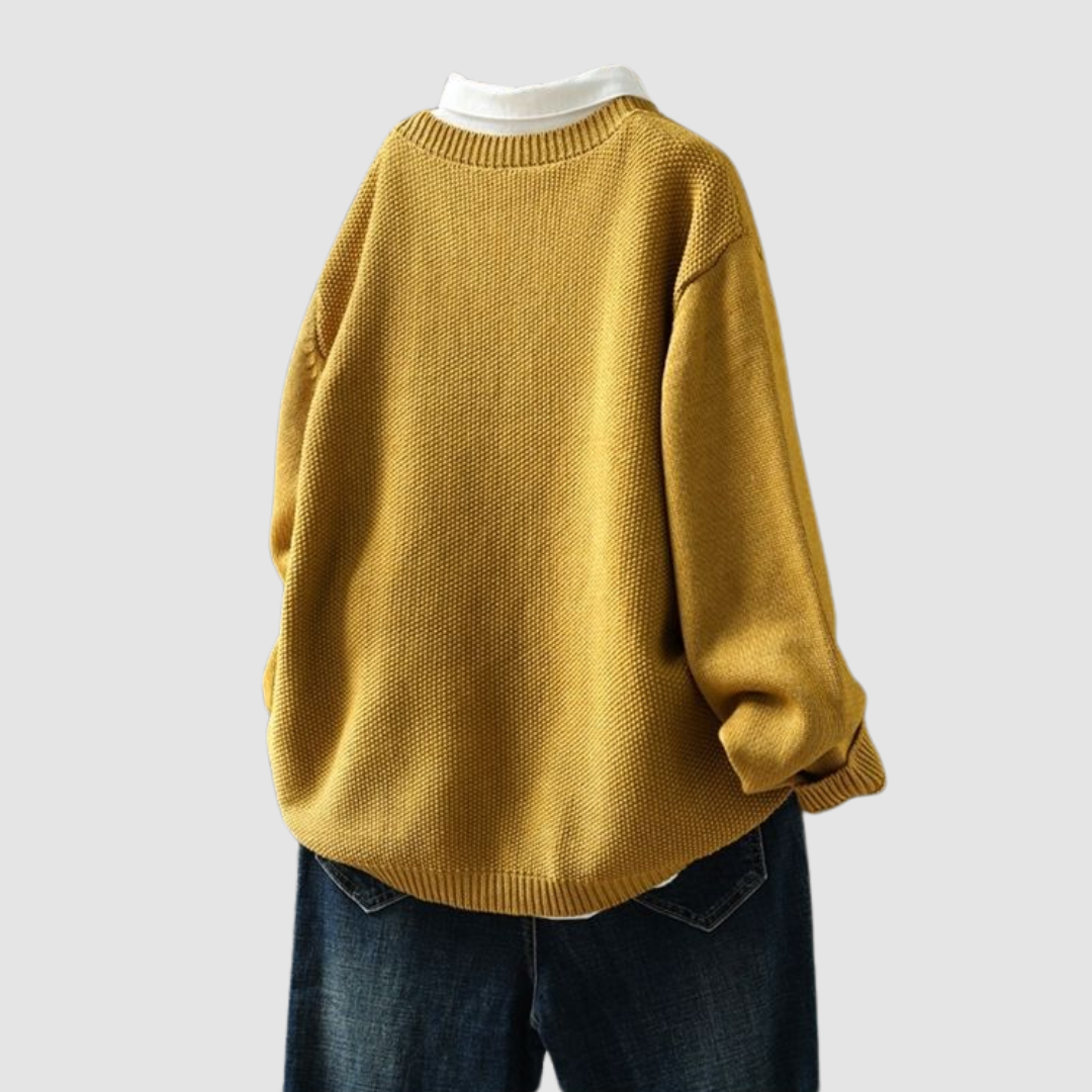 Back view of mustard knit cardigan on hanger over white shirt and dark jeans, light gray background.