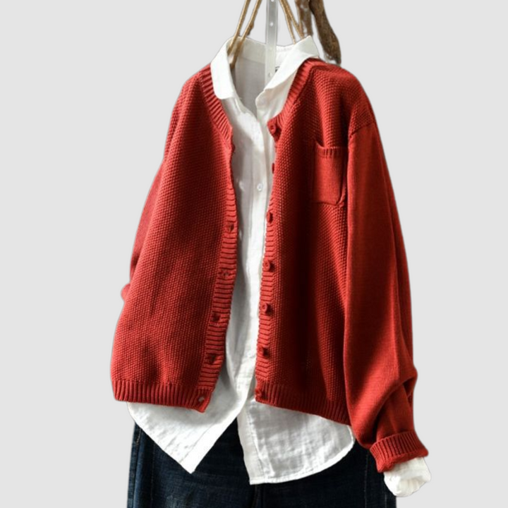 Red knit cardigan on hanger over white shirt and dark jeans against a light gray background.