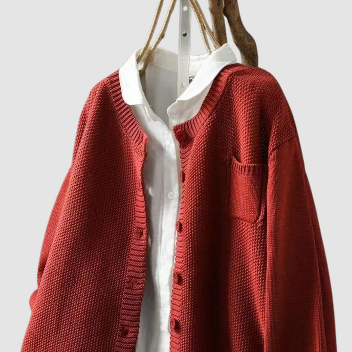 Close-up of red knit cardigan on hanger with button detail, light gray background.