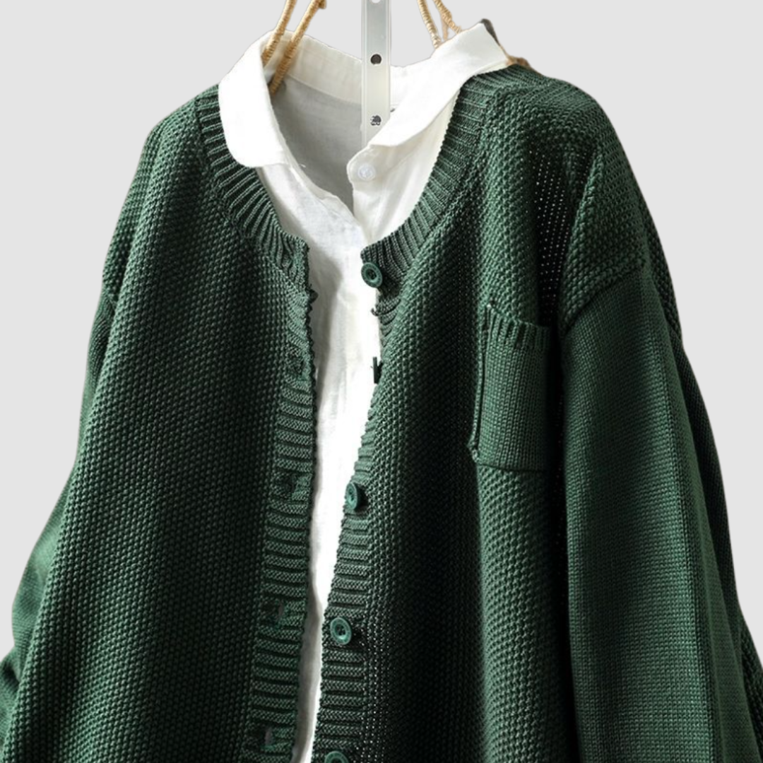 Close-up of dark green knit cardigan on hanger with button detail, light gray background.