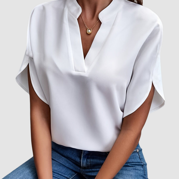 White draped blouse with a sleek V-neck and flowing short sleeves, worn with blue jeans, in a neutral studio setting.