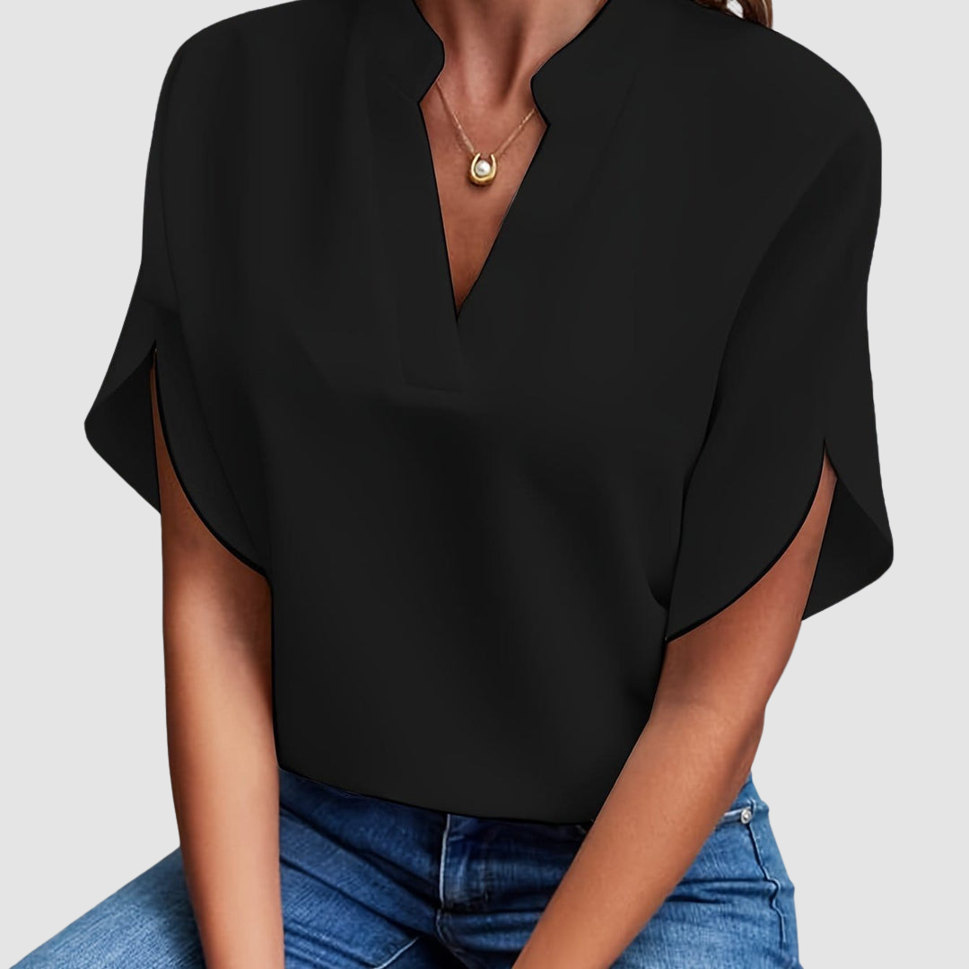 Black draped blouse with a sleek V-neck and flowing short sleeves, worn with blue jeans, in a neutral studio setting.