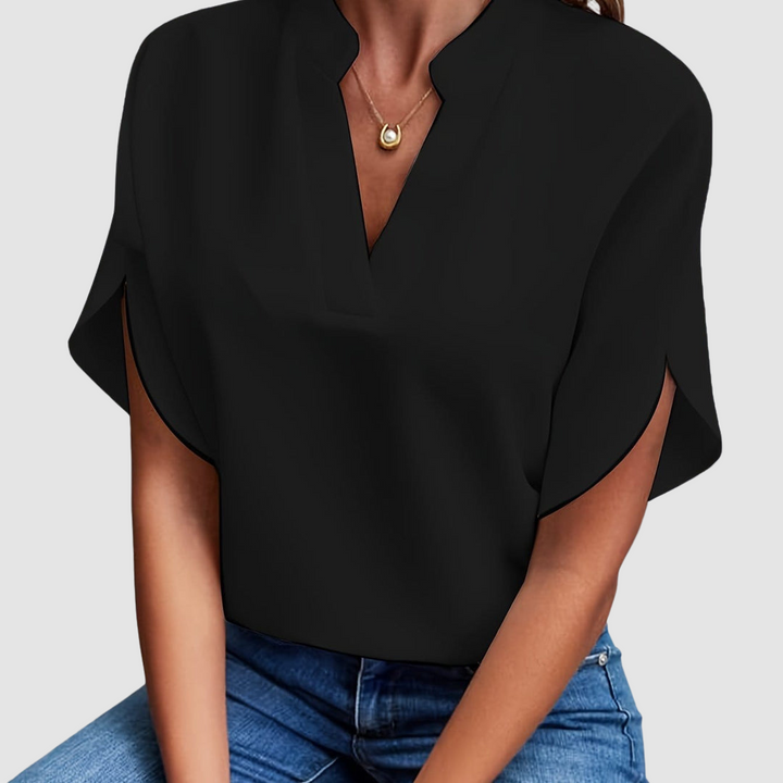 Black draped blouse with a sleek V-neck and flowing short sleeves, worn with blue jeans, in a neutral studio setting.