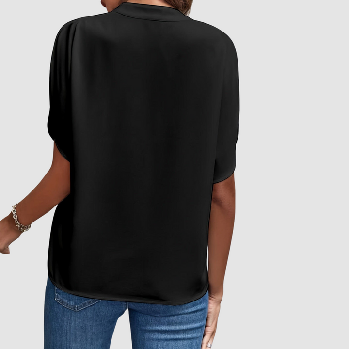 Back view of a black draped blouse, showcasing smooth, flowing fabric and easy fit, paired with blue jeans, studio setting.
