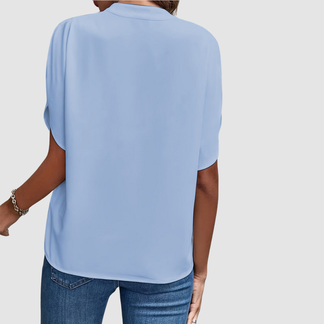 Back view of a light blue draped blouse, showcasing smooth, flowing fabric and easy fit, paired with blue jeans, studio setting.