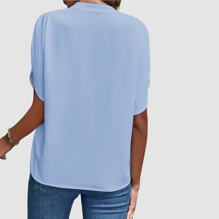 Back view of a light blue draped blouse, showcasing smooth, flowing fabric and easy fit, paired with blue jeans, studio setting.