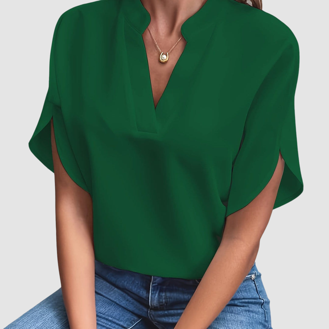 Green draped blouse with a sleek V-neck and flowing short sleeves, worn with blue jeans, in a neutral studio setting.