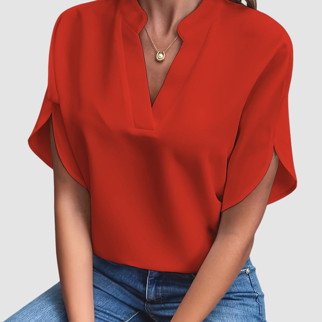 Red draped blouse with a sleek V-neck and flowing short sleeves, worn with blue jeans, in a neutral studio setting.